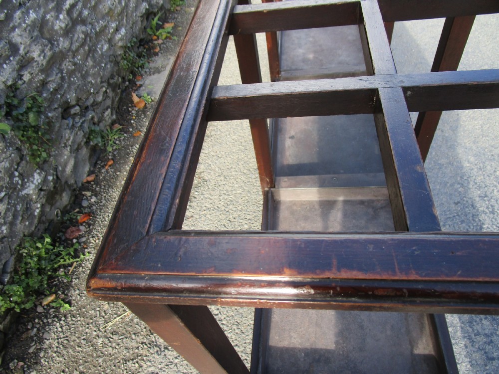 A long, dark wood stick stand featuring a grid of rectangular compartments at the top and sectioned metal drip trays at the base. View VI