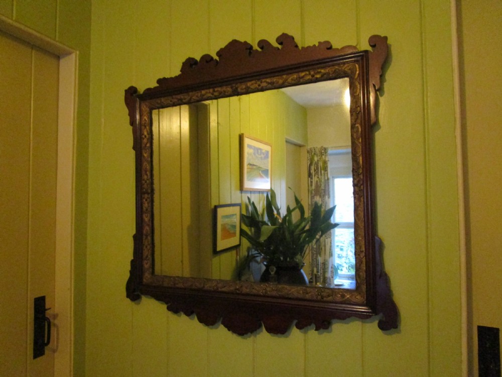 A rectangular mahogany wall mirror featuring decorative fretwork scroll cresting and an inner gilded floral slip.