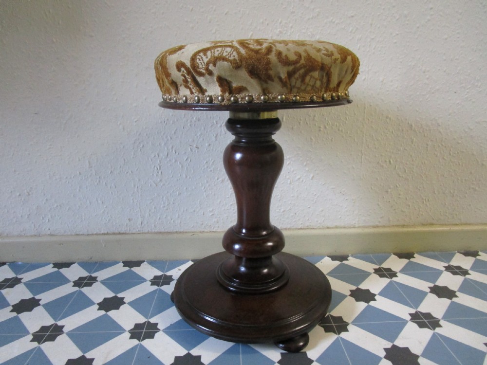 A Victorian dark wood revolving piano stool featuring a circular patterned velvet cushion trimmed with brass studs set atop a turned pedestal base.