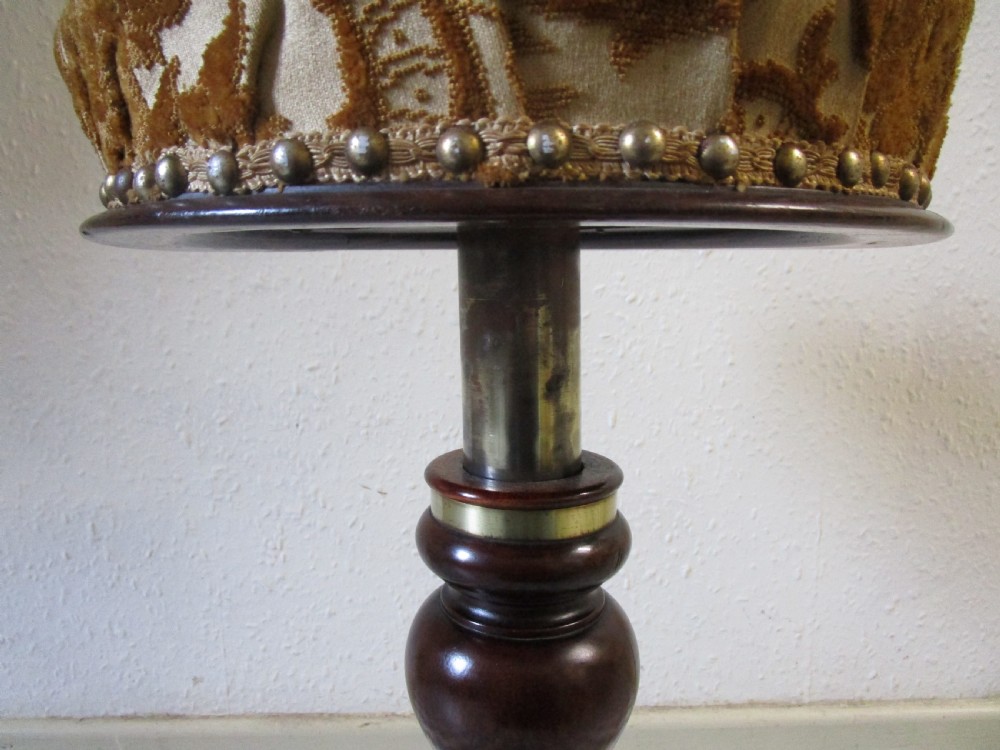A Victorian dark wood revolving piano stool featuring a circular patterned velvet cushion trimmed with brass studs set atop a turned pedestal base. View IV
