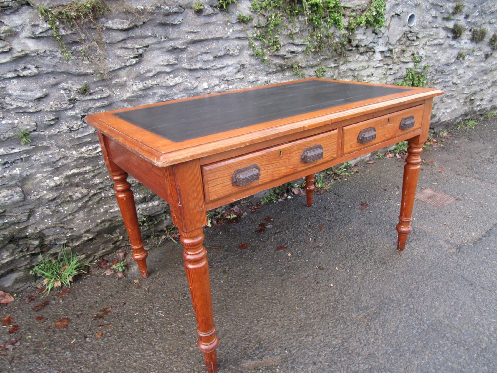 A warm brown pine writing table featuring a dark leather insert writing surface, two frieze drawers with decorative metal handles, and four turned legs. View II