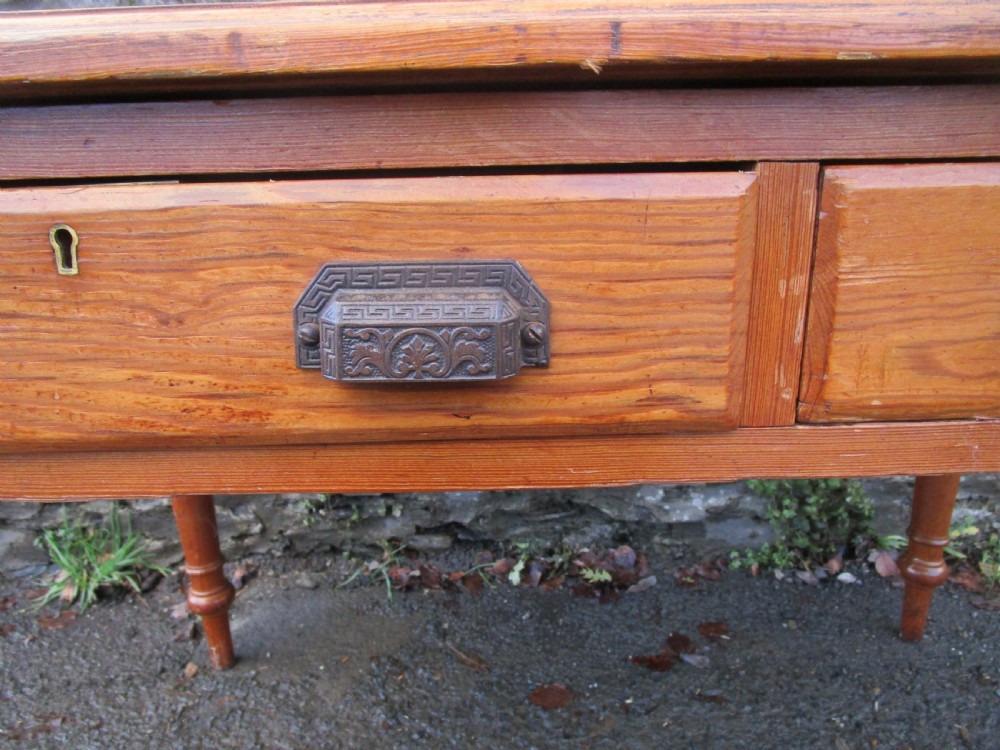A warm brown pine writing table featuring a dark leather insert writing surface, two frieze drawers with decorative metal handles, and four turned legs. View III