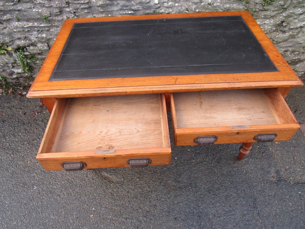 A warm brown pine writing table featuring a dark leather insert writing surface, two frieze drawers with decorative metal handles, and four turned legs. View IV