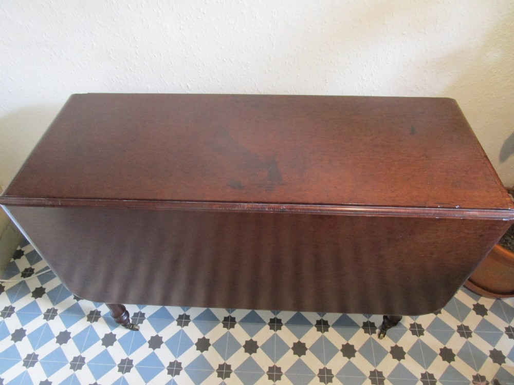 A Georgian plum pudding mahogany drop-leaf dining table with turned legs and brass castors. View II