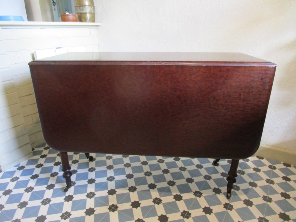 A Georgian plum pudding mahogany drop-leaf dining table with turned legs and brass castors. View IV
