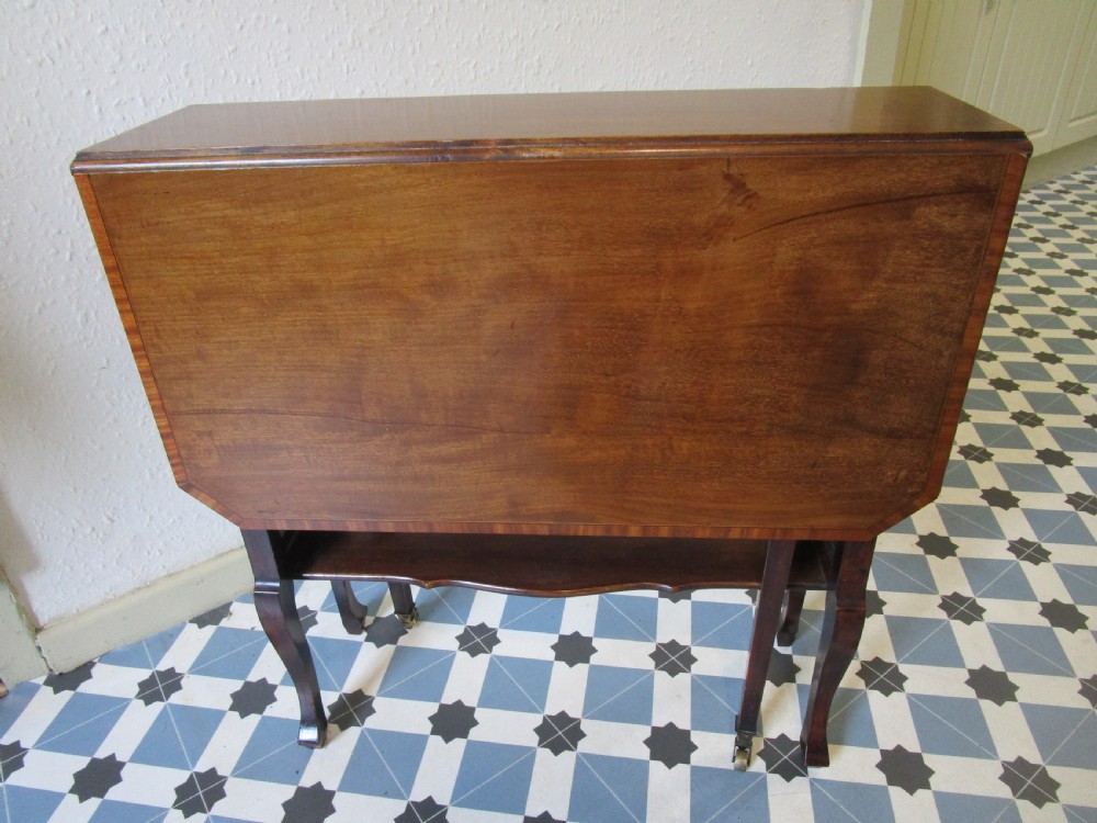 A compact mahogany Sutherland drop-leaf table with curved legs, a lower shelf, and small brass castors.