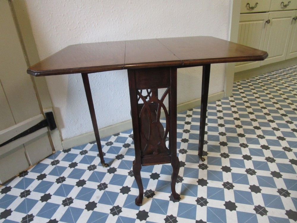 A compact mahogany Sutherland drop-leaf table with curved legs, a lower shelf, and small brass castors. View III