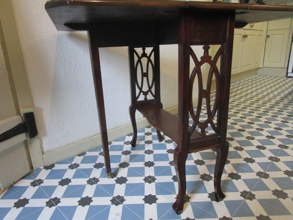 A compact mahogany Sutherland drop-leaf table with curved legs, a lower shelf, and small brass castors. View IV