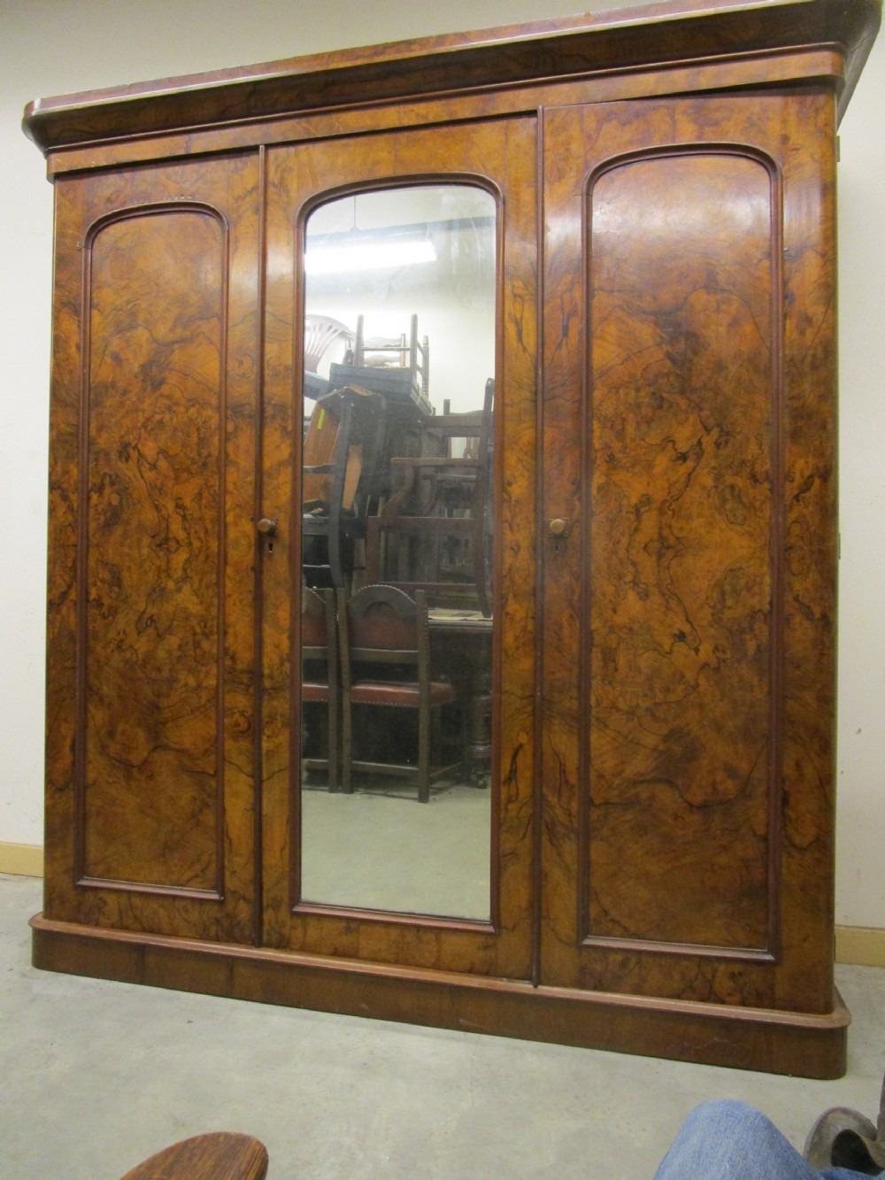 A Victorian three-door burr walnut compactum wardrobe featuring a full-length central mirror and arched panel doors set on a plinth base.