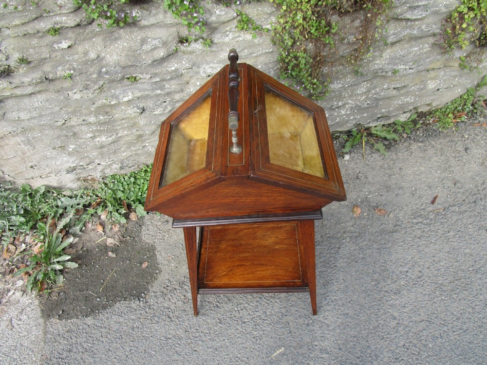An antique mahogany bijouterie table featuring a pitched glazed display lid with a central turned handle, boxwood inlay, and a lower shelf.