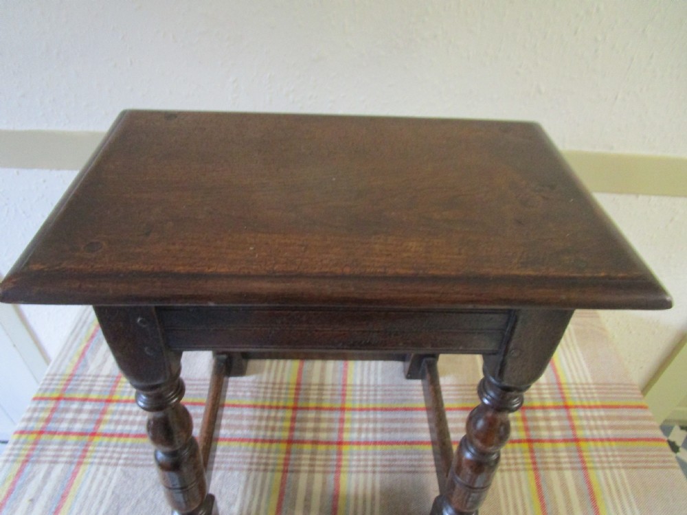 A dark oak joint stool featuring a rectangular top with moulded edges, turned baluster legs, and wooden peg joinery.