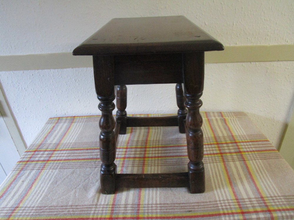 A dark oak joint stool featuring a rectangular top with moulded edges, turned baluster legs, and wooden peg joinery. View II