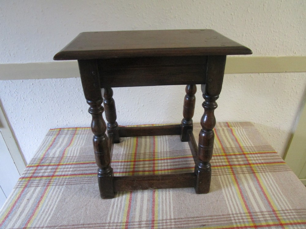 A dark oak joint stool featuring a rectangular top with moulded edges, turned baluster legs, and wooden peg joinery. View IV
