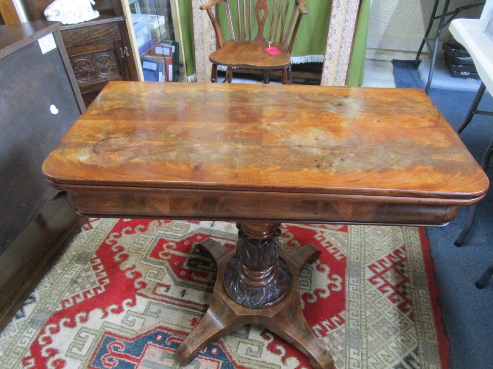 An antique timber fold-over tea table featuring a figured veneer top and a central carved pedestal base on four shaped legs.