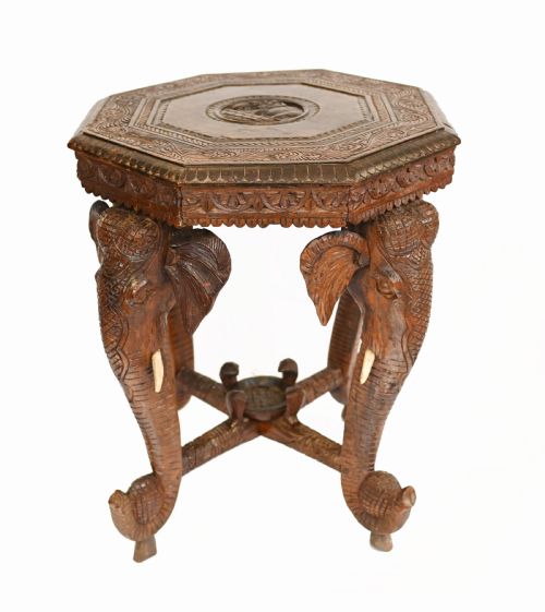 fig 1. An octagonal carved wooden side table featuring three legs sculpted in the shape of elephant heads with trunks curving down to form the feet.