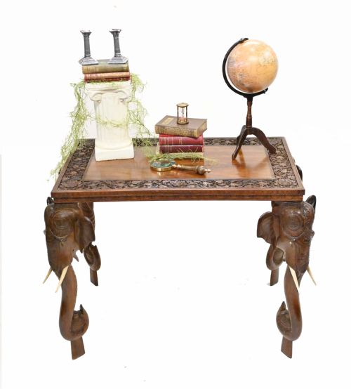fig 1. A dark timber rectangular side table featuring a carved foliage border and four legs sculpted as elephant heads with trunks extending to the floor.