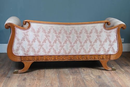 fig 1. A Regency carved walnut sofa featuring scrolled arms, anthemion leaf relief carving along the apron frieze, pink patterned upholstery, and matching bolster cushions.