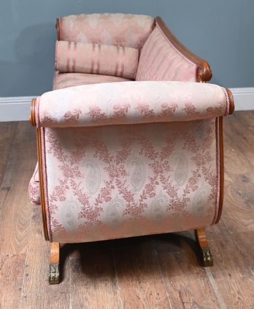 fig 3. A Regency carved walnut sofa featuring scrolled arms, anthemion leaf relief carving along the apron frieze, pink patterned upholstery, and matching bolster cushions.