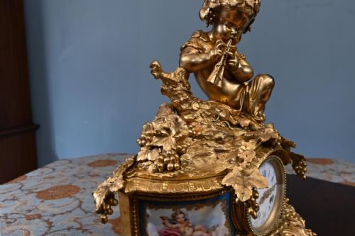 fig 1. A late 19th-century French Rococo gilt bronze mantel clock featuring a sculpted cherub playing a pipe atop, flanked by sky-blue painted porcelain plaques.