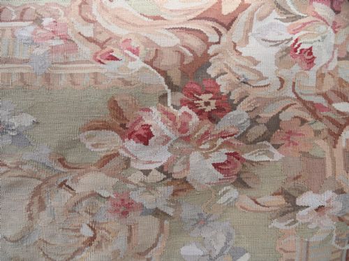 fig 2. A large rectangular French Aubusson style flat-weave tapestry featuring a central floral bouquet medallion surrounded by scrolling foliate borders in pink, beige, and muted green shades.