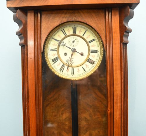 fig 1. An antique walnut Vienna regulator wall clock featuring a glazed front door, brass pendulum, and turned bottom finials.