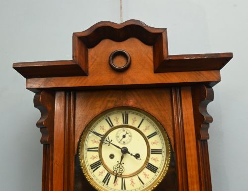 fig 2. An antique walnut Vienna regulator wall clock featuring a glazed front door, brass pendulum, and turned bottom finials.