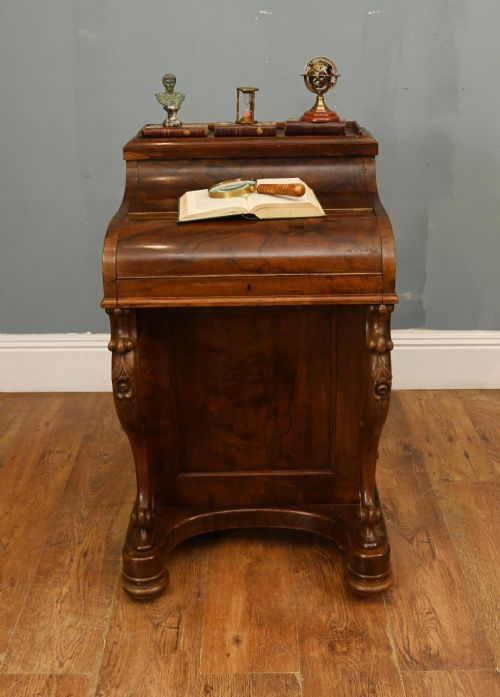 fig 2. A Victorian walnut Davenport desk featuring a sloped piano-style lid, carved cabriole supports, and a rich wood grain finish.