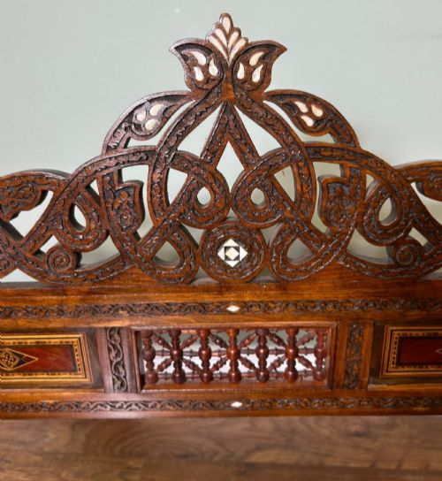 fig 2. A pair of warm brown wooden armchairs featuring elaborate carved openwork crestings and geometric mother-of-pearl inlays across the seats and panels.
