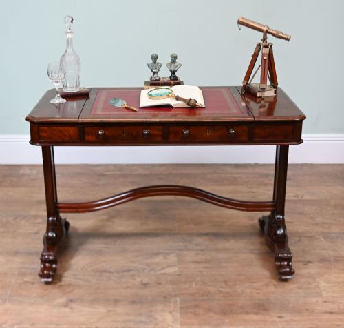 fig 1. A late Victorian mahogany writing table featuring a central red leather skiver with gold tooling, two frieze drawers, turned end supports, and a curved stretcher.