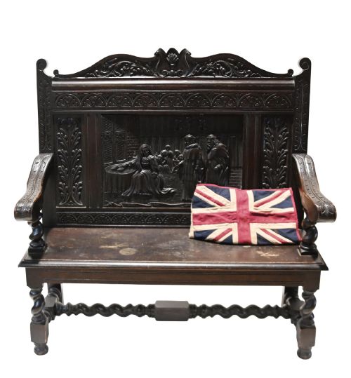 fig 1. A late 19th-century dark carved walnut hall bench featuring a pictorial relief back panel, scrolled armrests, and turned stretchers.