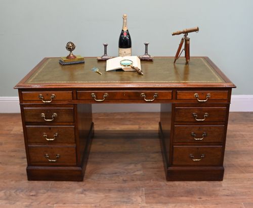 fig 1. A Victorian mahogany pedestal desk featuring nine brass-handled drawers and a green leather gilt-tooled writing surface resting on a solid plinth base.