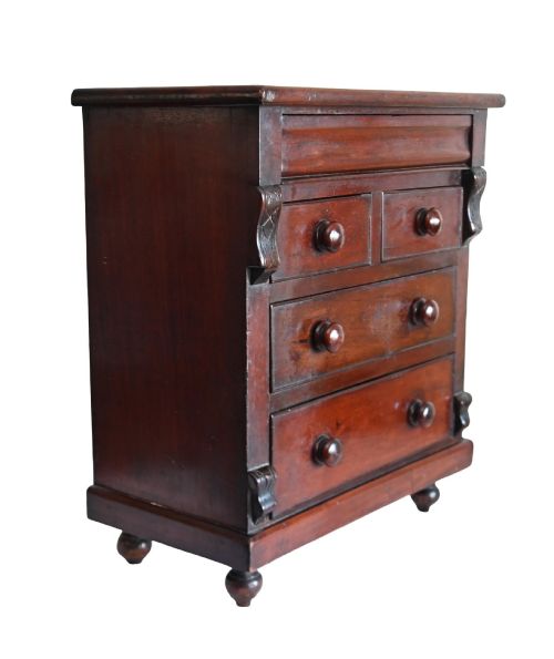 fig 3. A 19th-century Scottish mahogany miniature apprentice chest featuring two short over two long drawers, a top cushion drawer, turned knobs, carved corbels, and turned feet.