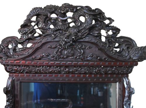 fig 1. An intricately carved dark hardwood Japanese Meiji display cabinet featuring a dragon pediment, glazed door, and tiered asymmetrical shelves.
