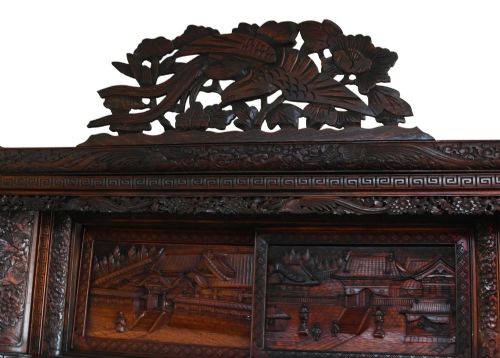 fig 2. An intricately carved dark brown Japanese Meiji period display cabinet featuring asymmetrical open shelves, relief-carved cupboard doors, and a decorative cresting piece.