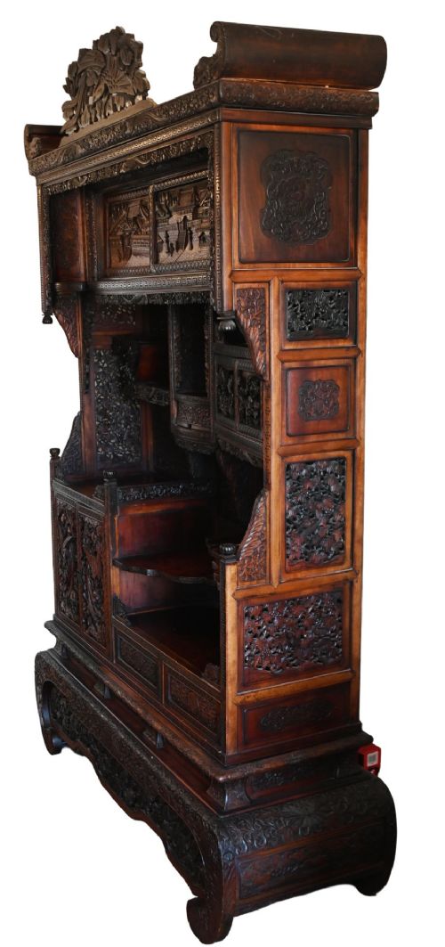 An intricately carved dark brown Japanese Meiji period display cabinet featuring asymmetrical open shelves, relief-carved cupboard doors, and a decorative cresting piece. View XIV