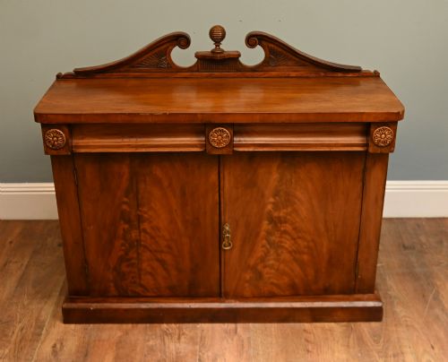 fig 1. A William IV mahogany chiffonier side cabinet featuring a scroll-carved back gallery, central turned finial, carved rosette accents, and twin flame mahogany cupboard doors.