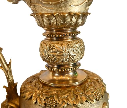 fig 1. A pair of 19th-century French gilt bronze ewers featuring detailed Bacchus relief scenes, leaf motifs, and cherub-topped handles.
