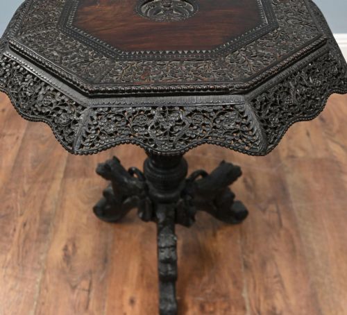 fig 2. An antique octagonal dark hardwood side table featuring intricate pierced floral carvings around the apron and a central turned pedestal supported by three mythical carved beast legs.