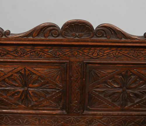 fig 2. A Victorian dark oak carved settle featuring carved lion head armrests, detailed floral and geometric back panels, and a lift-up storage seat.