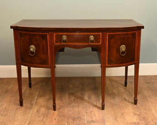 fig 1. An Edwardian mahogany bowfront sideboard with satinwood inlaid borders, three central drawer and cabinet sections, and brass lion mask ring handles on tapered legs.