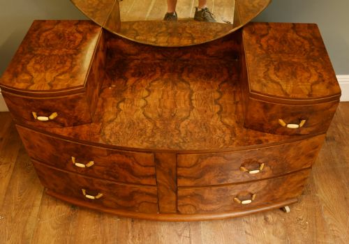 fig 1. An Art Deco burr walnut dressing table featuring a large circular mirror mounted behind six bow-fronted drawers.