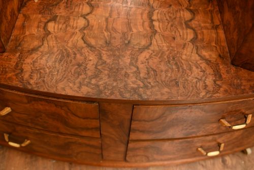 fig 2. An Art Deco burr walnut dressing table featuring a large circular mirror mounted behind six bow-fronted drawers.