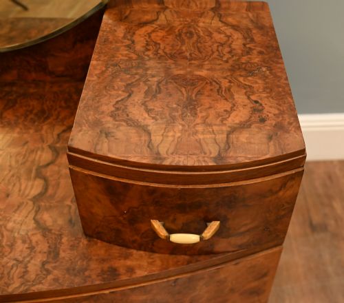 fig 3. An Art Deco burr walnut dressing table featuring a large circular mirror mounted behind six bow-fronted drawers.