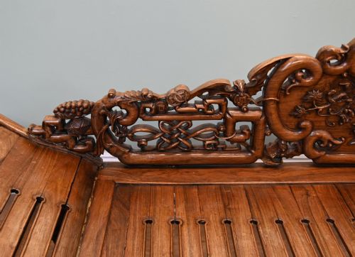fig 4. An intricately hand-carved warm brown hardwood Chinese opium bench featuring a slatted seat, elevated recline end, and pierced scrollwork along the backrest.