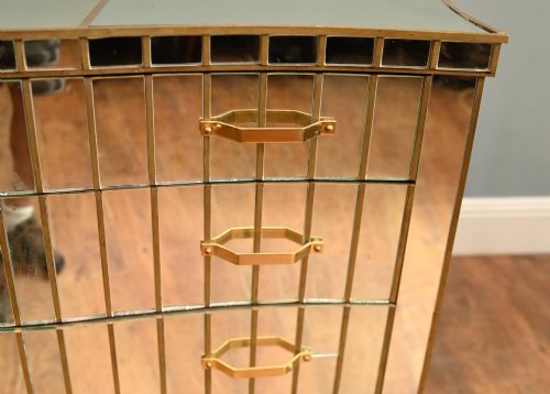 fig 2. An Art Deco mirrored chest of drawers featuring segmented glass panelling, four drawers with geometric brass handles, and a shaped lower apron.