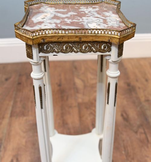 fig 2. A white painted tall French pedestal stand featuring four fluted legs, gilt brass mounts, a lower tier, and a shaped variegated marble top with a brass gallery.