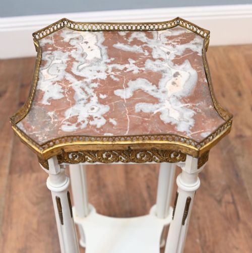 fig 3. A white painted tall French pedestal stand featuring four fluted legs, gilt brass mounts, a lower tier, and a shaped variegated marble top with a brass gallery.