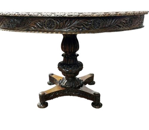 fig 2. A round antique Burmese hardwood dining table featuring a polished top, an intricately carved apron, and a central pedestal base with tripod legs.