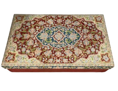 fig 1. A low rectangular ottoman featuring a central multi-coloured floral needlepoint tapestry top bordered by red velvet side fabric with a pull tab.