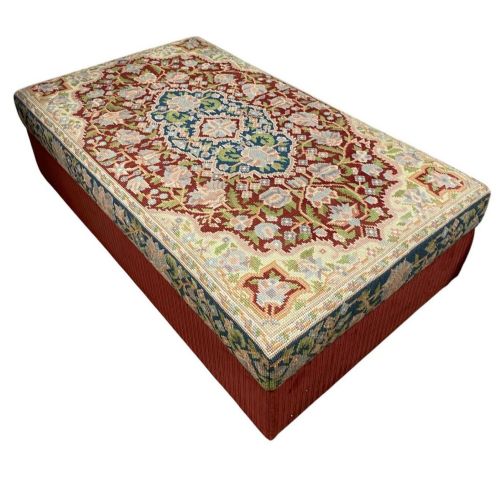 fig 2. A low rectangular ottoman featuring a central multi-coloured floral needlepoint tapestry top bordered by red velvet side fabric with a pull tab.